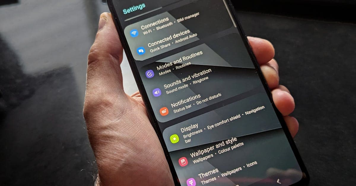 Hand holding smartphone displaying settings screen with various options evident.