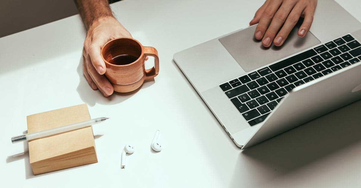 Minimalist workspace featuring a laptop, coffee mug, and AirPods for a modern work setup.