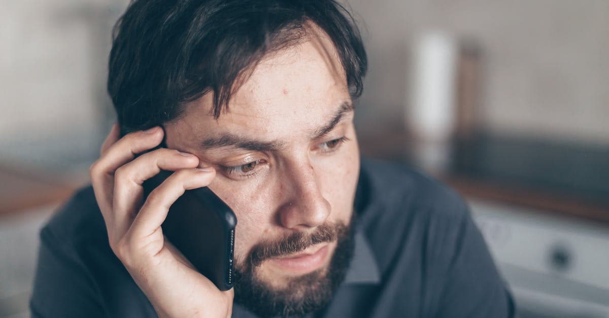Thoughtful bearded man using smartphone, sitting indoors with a concerned expression.