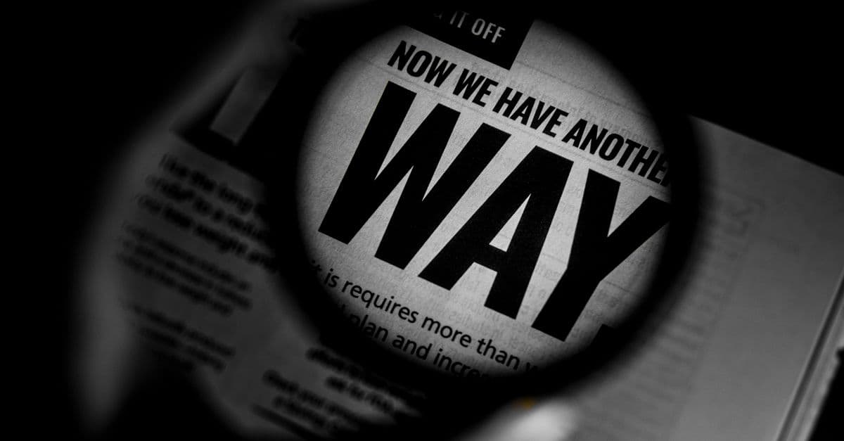 Black and white close-up of newspaper text magnified through a lens, emphasizing the word 'WAY'.