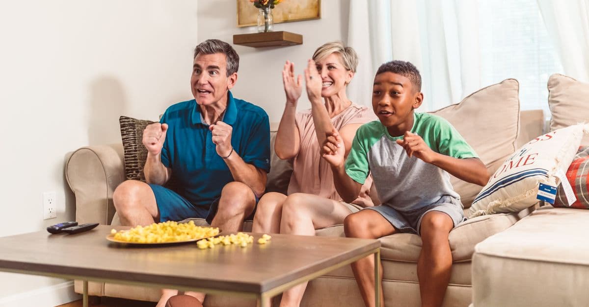 A joyful family bonding experience while watching TV and enjoying snacks on the sofa.