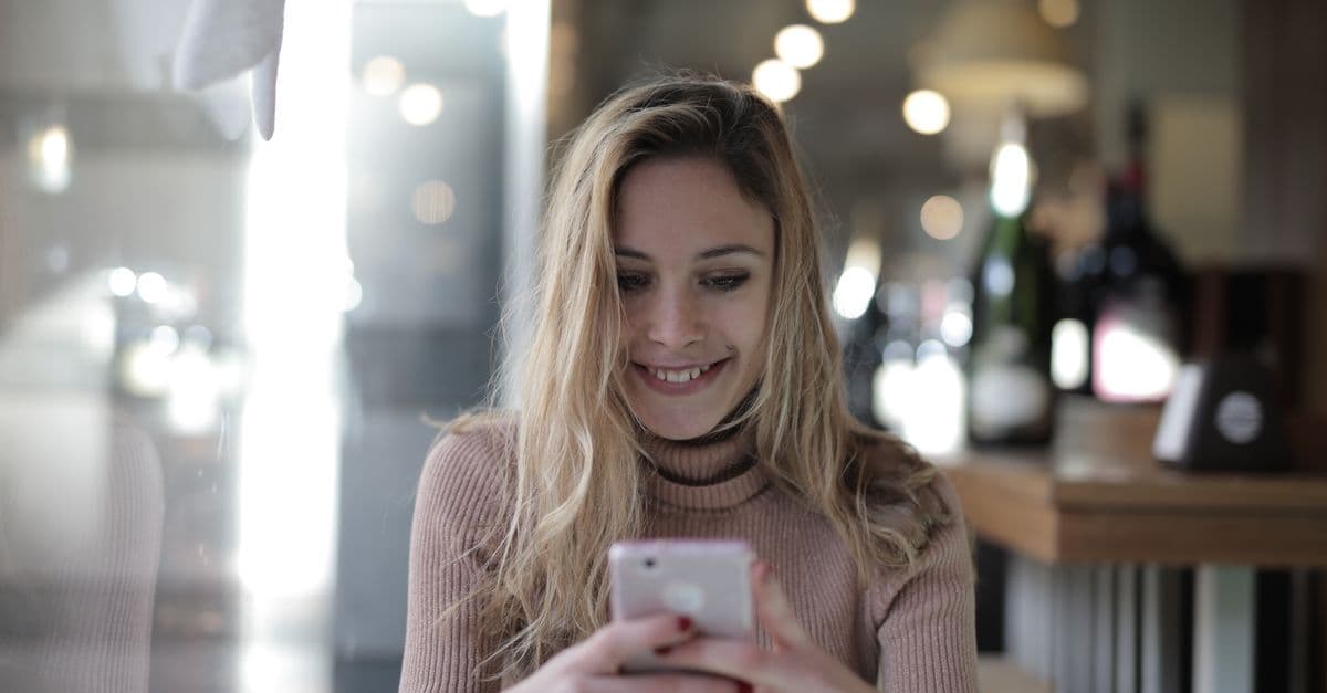 A joyful woman with blonde hair texting on her smartphone in a cozy cafe.