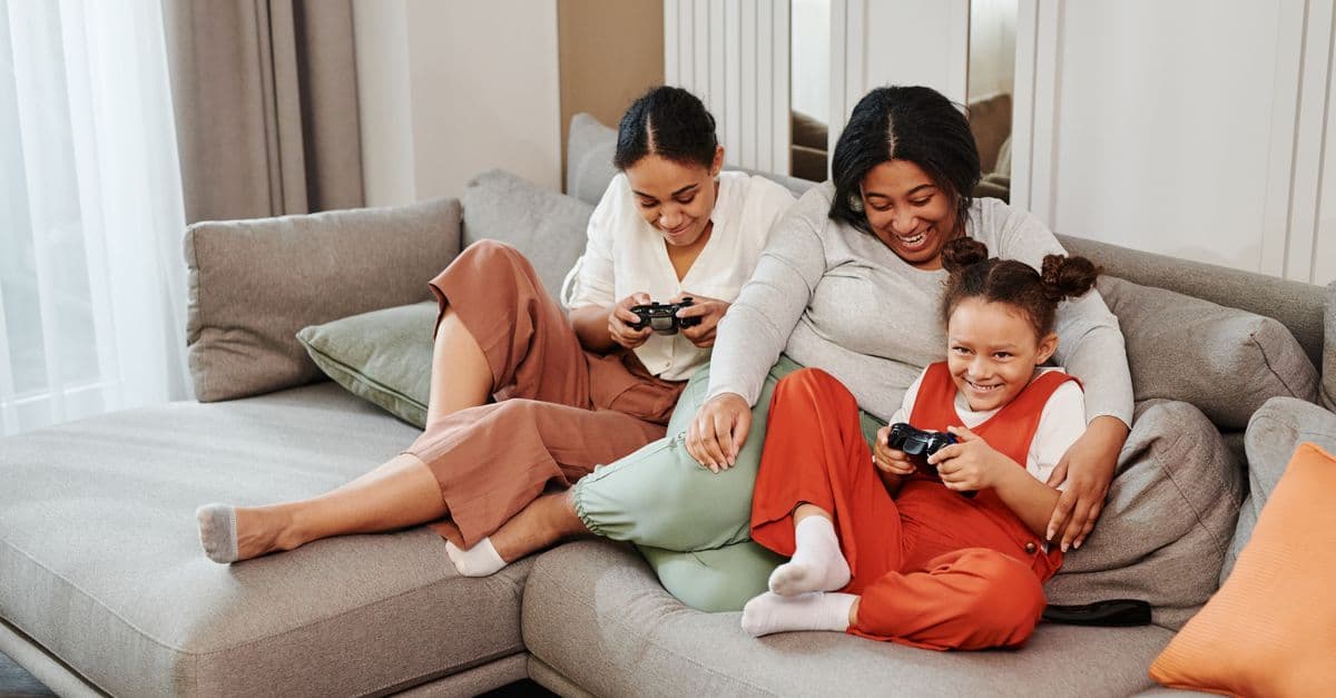 A joyful family moment as mother and daughters play video games together on the couch.