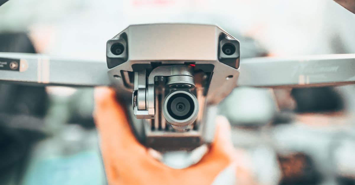 Crop unrecognizable person holding contemporary drone against blurred interior and demonstrating powerful camera