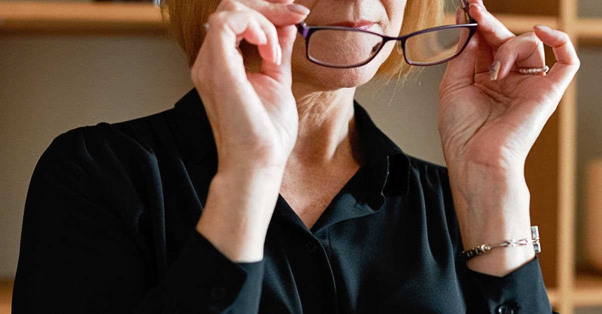 Close-up of businesswoman adjusting eyeglasses, showcasing a moment of focus and professionalism.