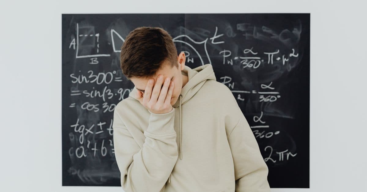 A frustrated student in a classroom standing in front of a blackboard filled with trigonometry equations.