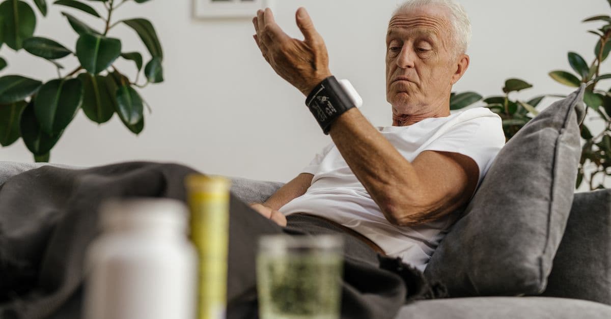 Elderly man checks his blood pressure using a wrist monitor in a comfortable living room setting.