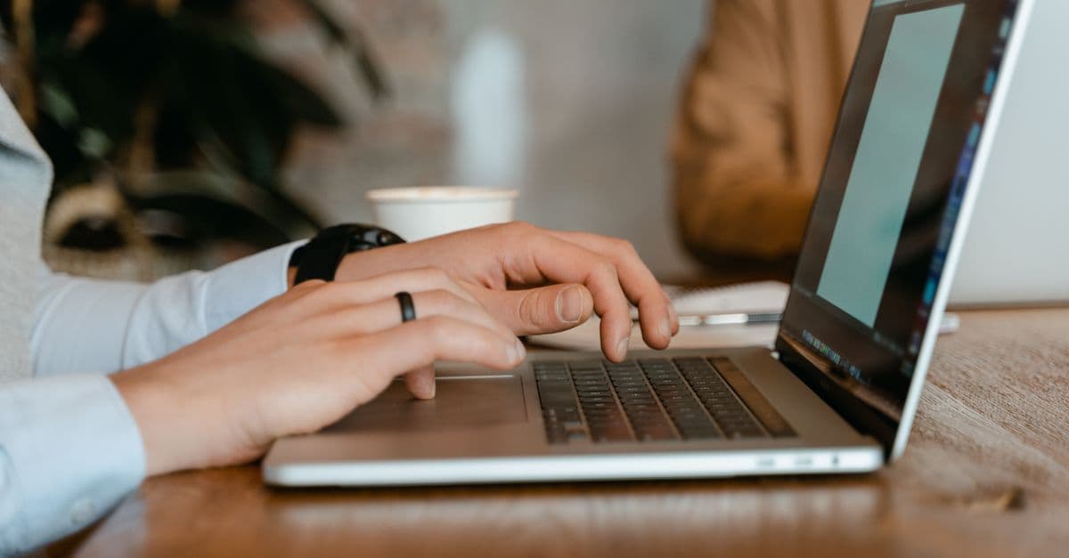A person typing on a laptop at a wooden table in a modern office setting.
