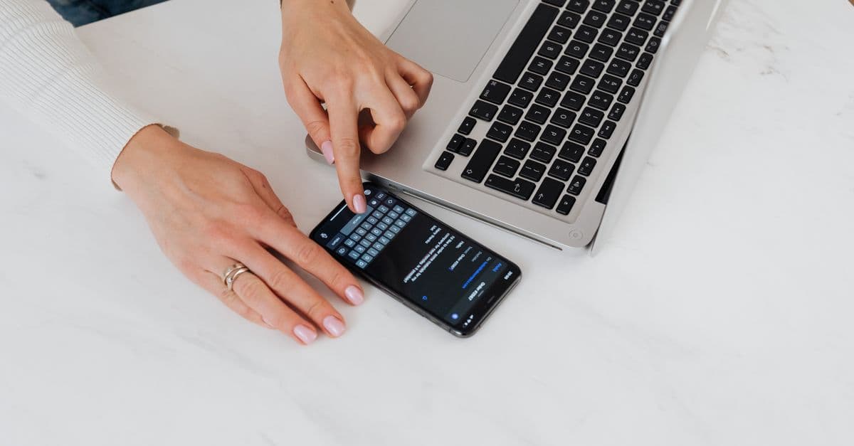 Close-up of hands using smartphone and laptop on a white desk. Perfect for tech and business concepts.
