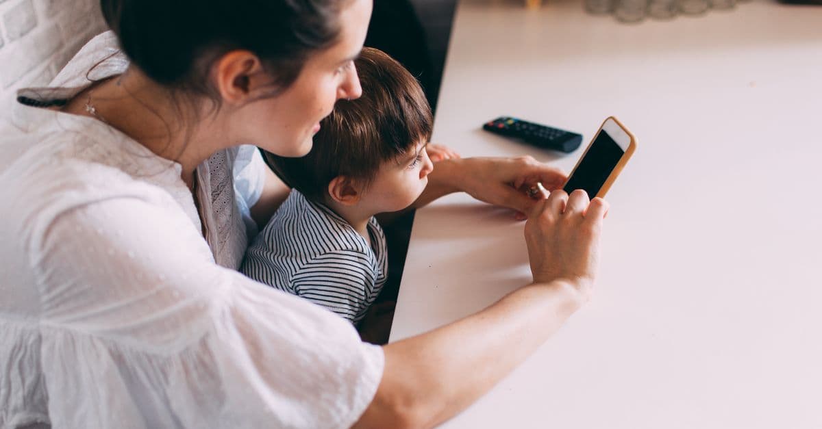 A mother and her child engaging with a smartphone indoors. Perfect for family and technology themes.