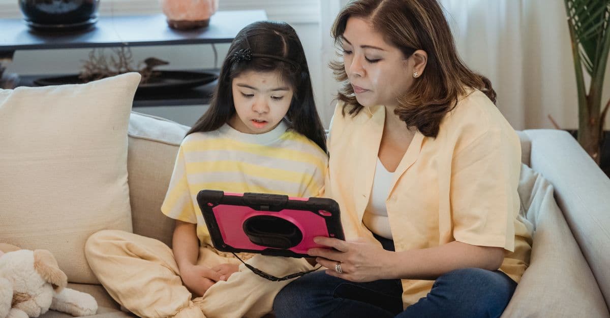 A mother and daughter bonding on the sofa using a tablet indoors.