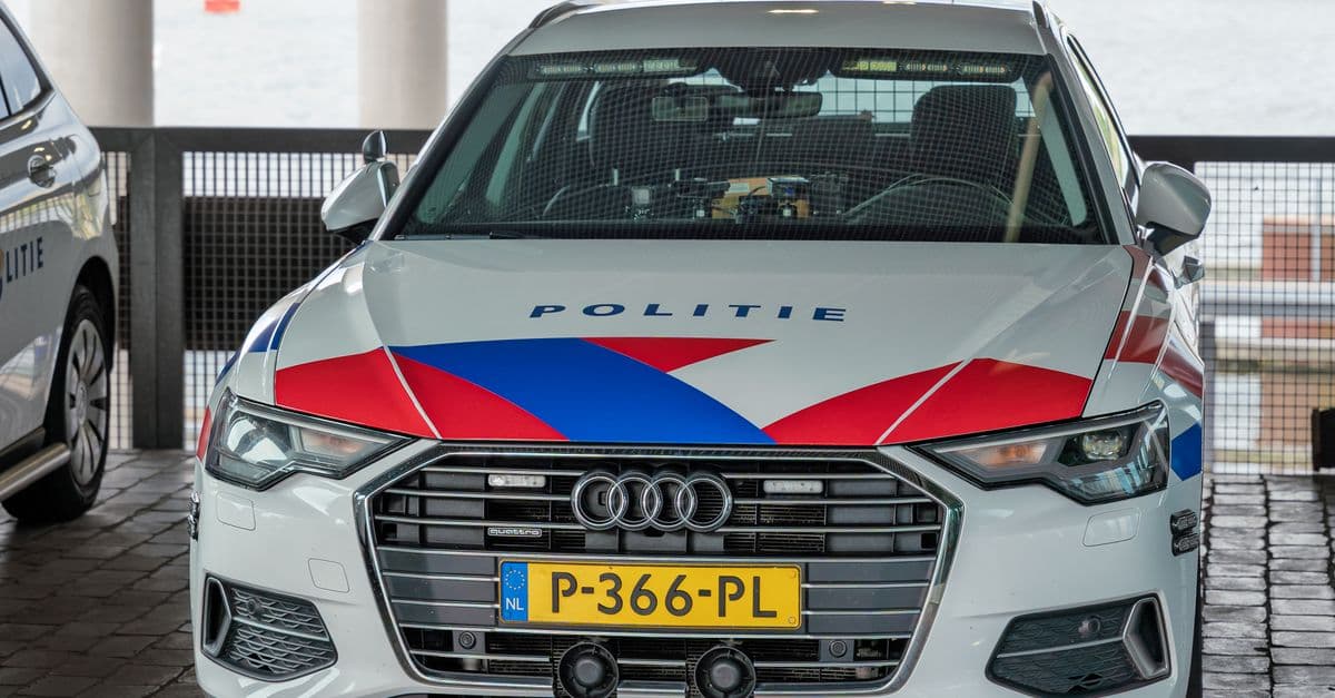 A Dutch police car with 'Politie' markings parked in an urban environment, displaying its distinctive red, white, and blue colors.