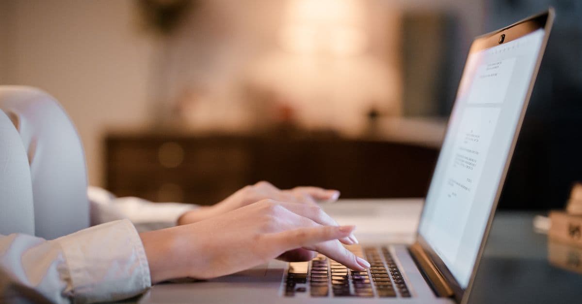 Close-up of hands typing on a laptop at home, showcasing a cozy work environment.