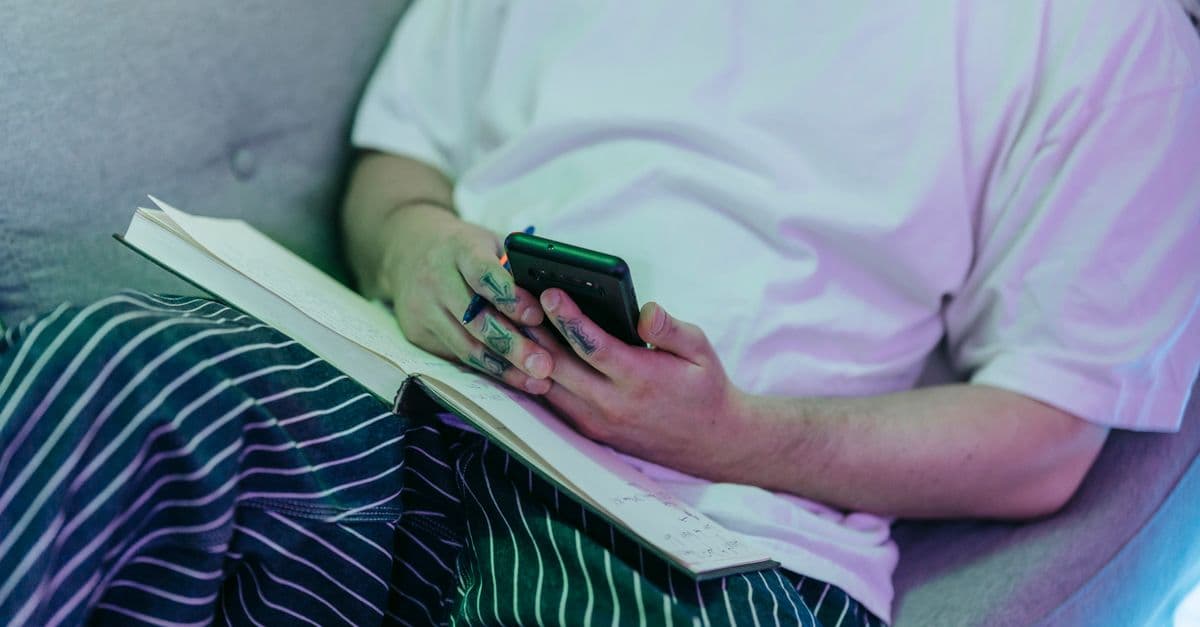 Seated individual holding a phone and pen, open notebook on lap.