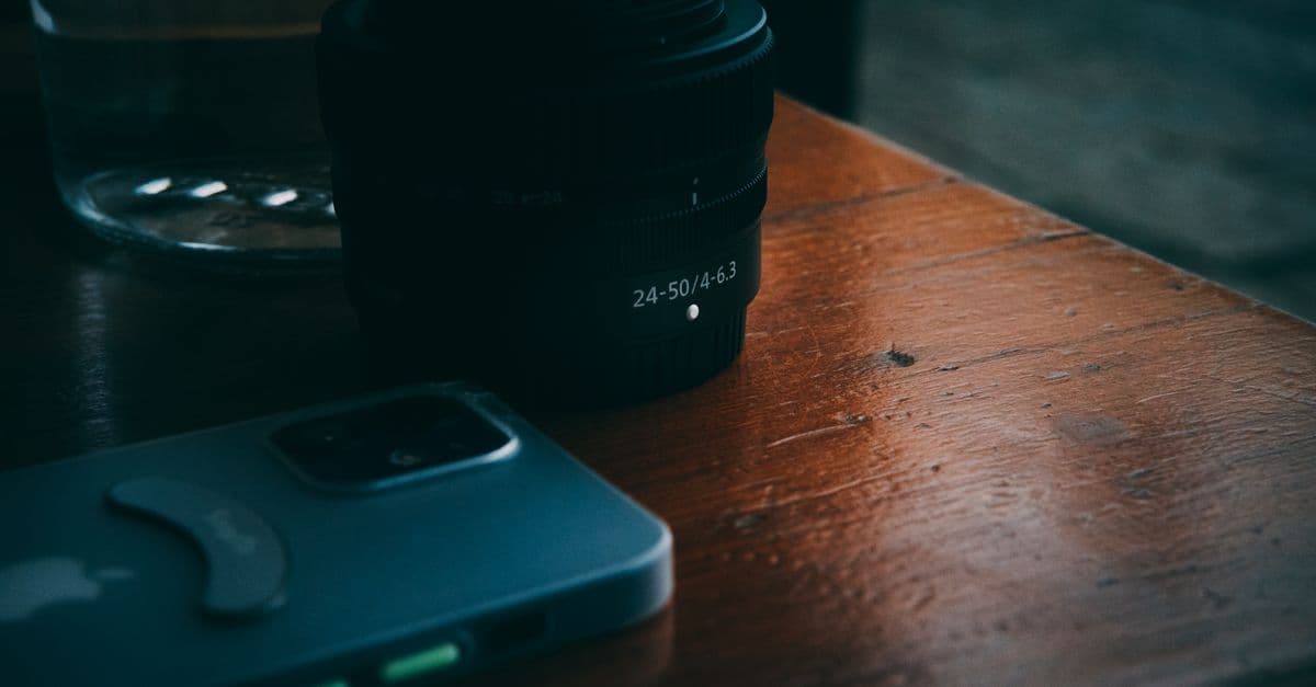 Camera lens and smartphone on a wooden table, capturing a still life technology scene.