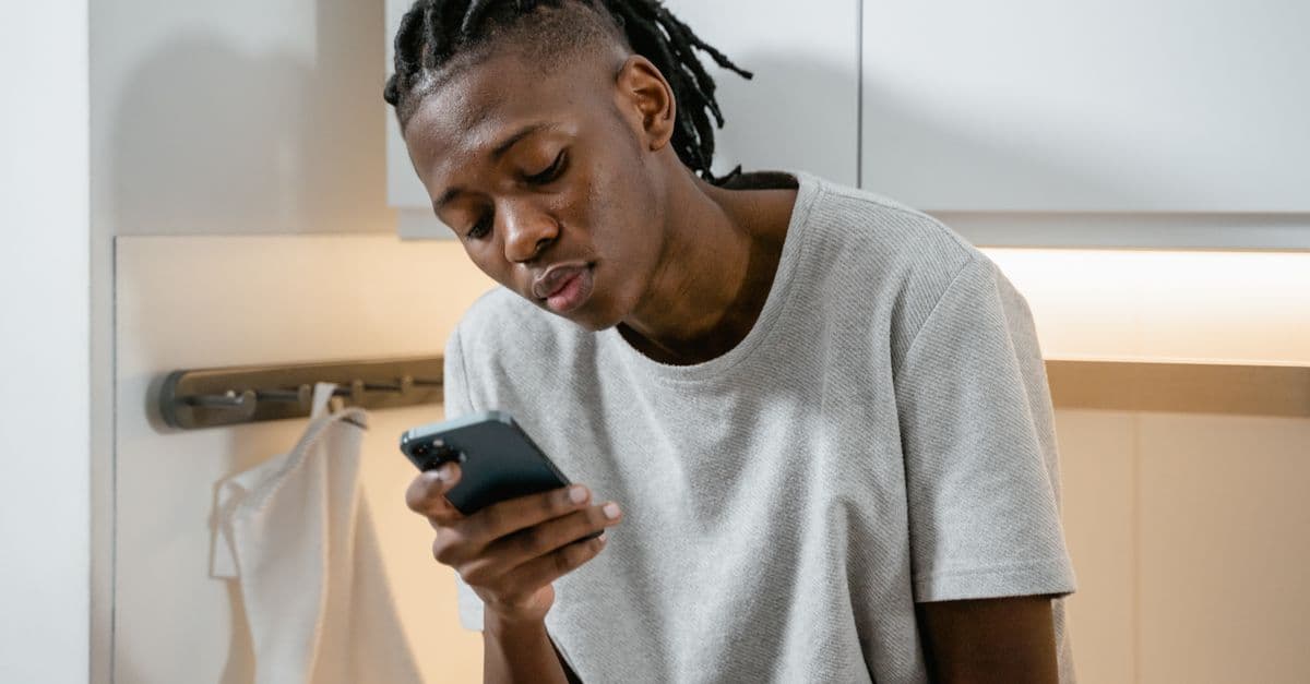 Focused individual texting on smartphone in modern kitchen environment.