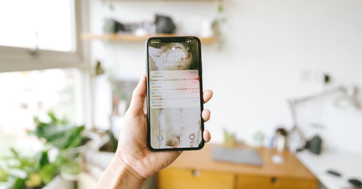 Hand holding smartphone indoors with blurred office background, focus on screen notifications.
