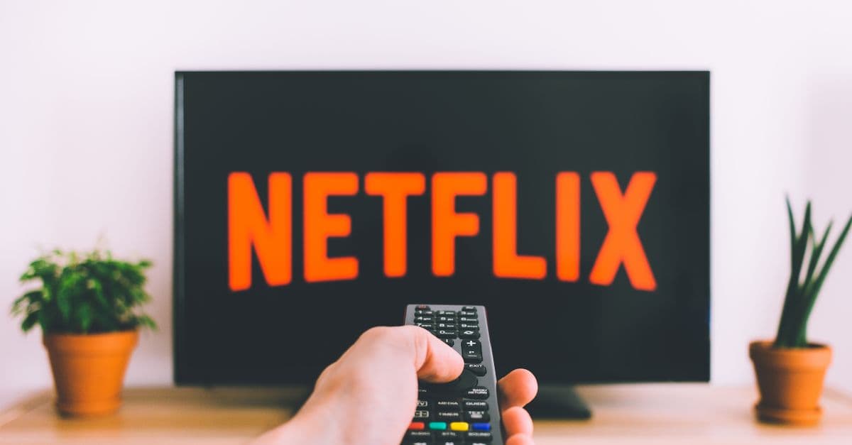 A hand holding a TV remote in front of a screen with Netflix, perfect for streaming and movie night themes.