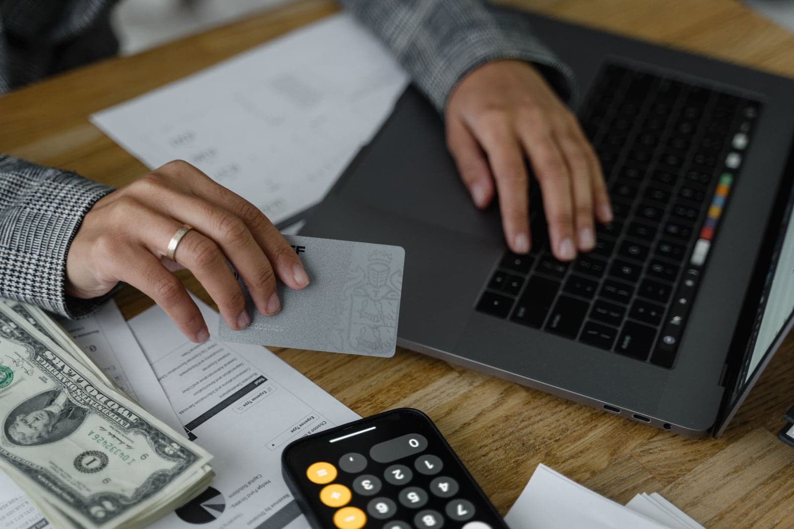 Person using a credit card at a laptop beside cash and a calculator