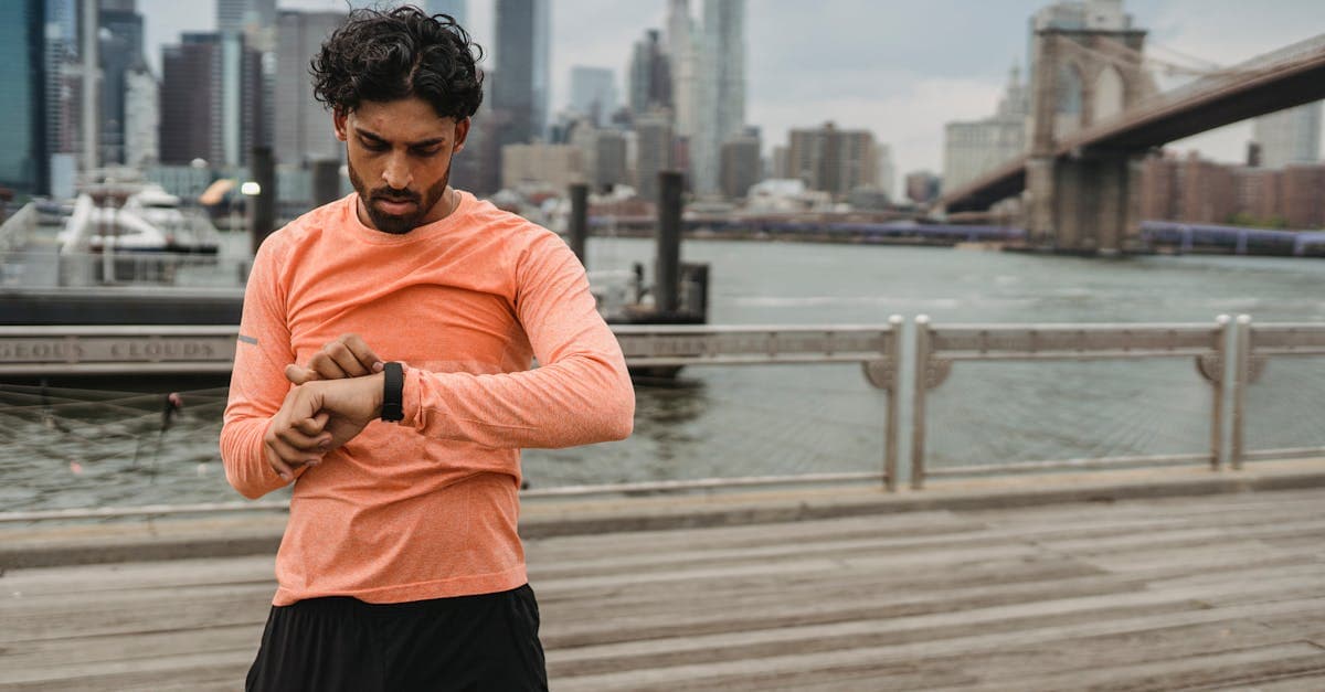 Adult man checks smartwatch while exercising by the Brooklyn Bridge, promoting healthy lifestyle.