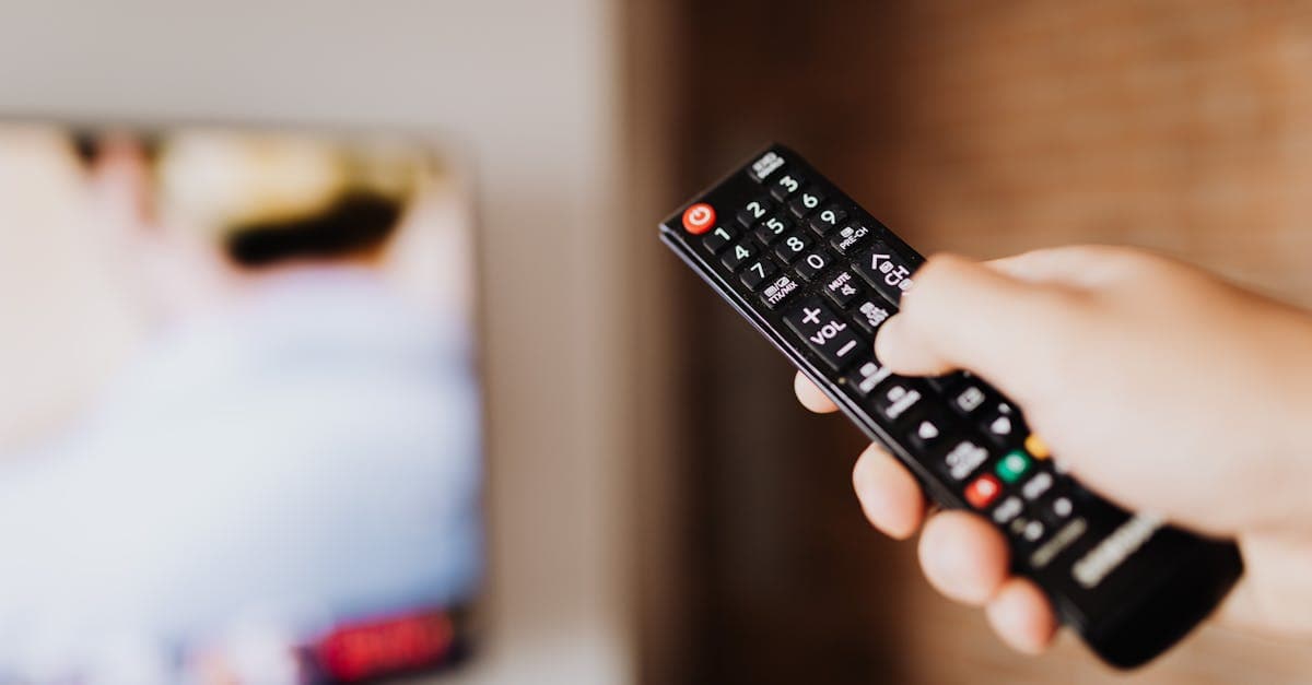 Close-up of a person using a TV remote with a blurred background indoors.