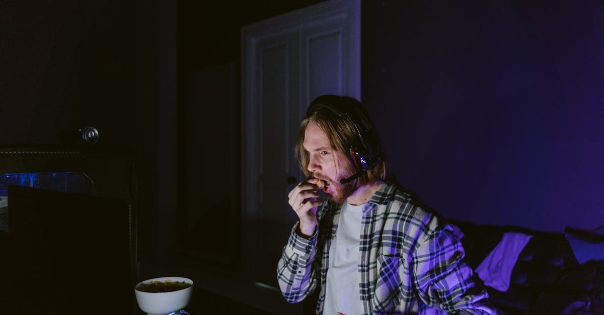 A man enjoying snacks while gaming in a dimly lit room, immersed in his screen.