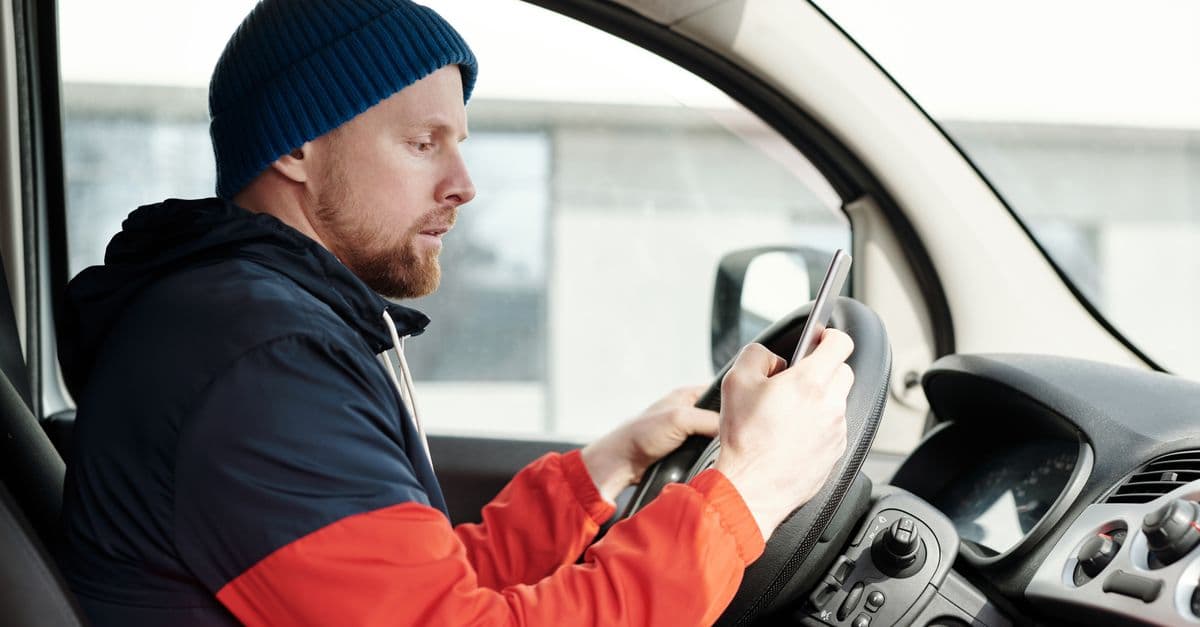 Distracted driver uses a smartphone in a car, highlighting road safety concerns.