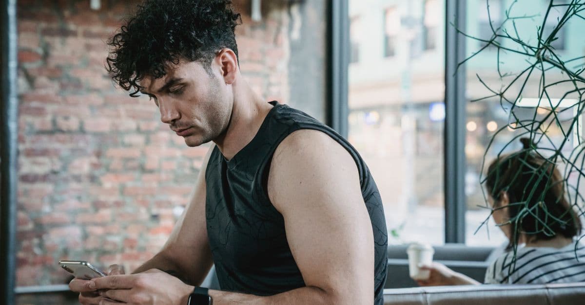 A man in activewear checks his smartphone in a cozy café setting.
