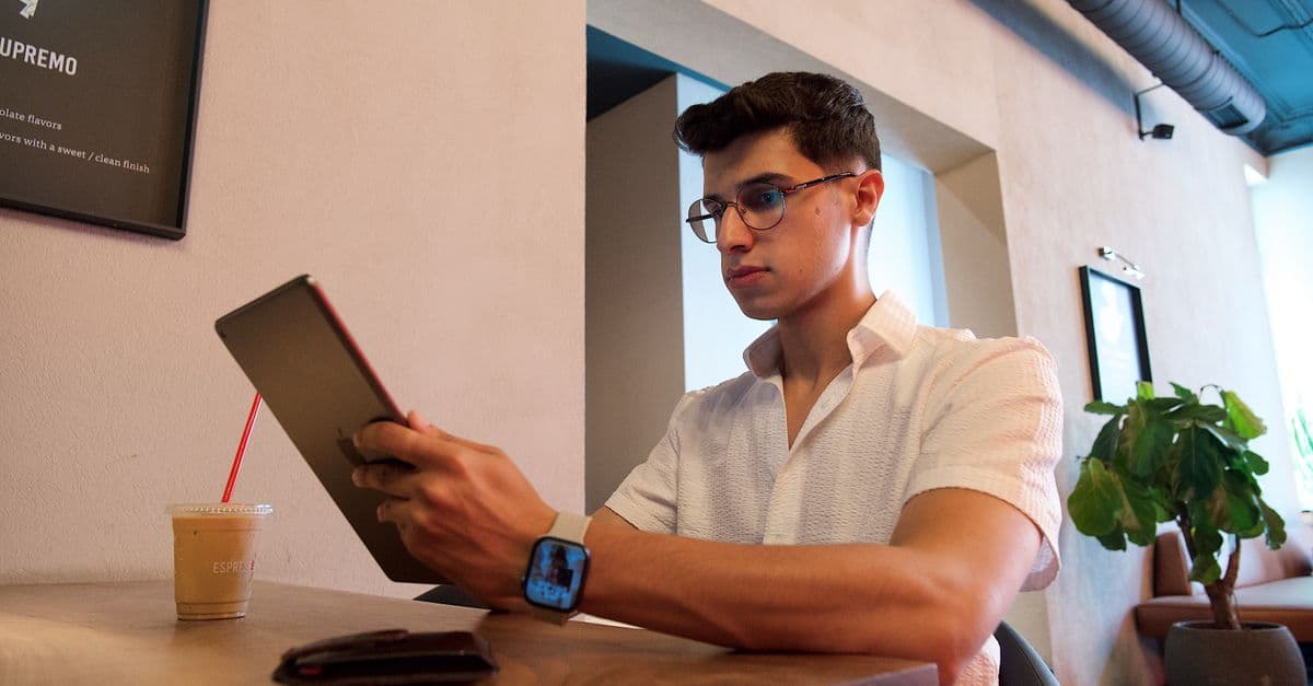 Young man in a café focused on a tablet, wearing a smartwatch.