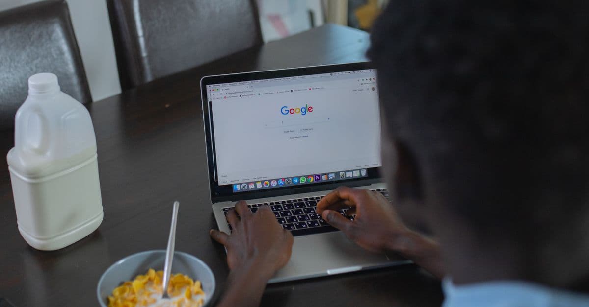 A person browsing Google on a laptop while having cereal breakfast at the table.