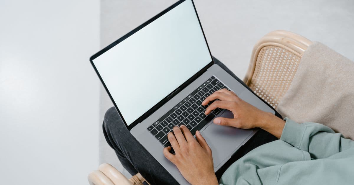 Overhead view of a person typing on a laptop in a comfortable armchair indoors.