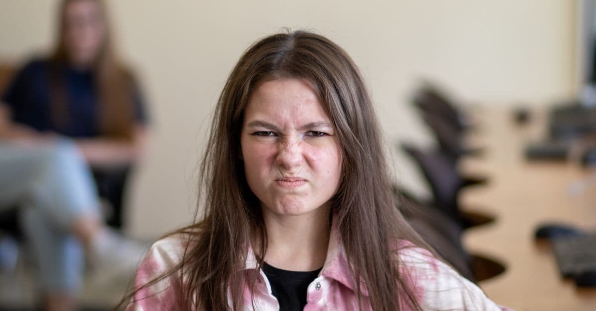 An angry teenage girl sitting in a classroom, displaying a frustrated expression.