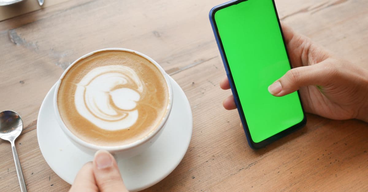 Close-up of a latte and a smartphone with a green screen on a wooden table.
