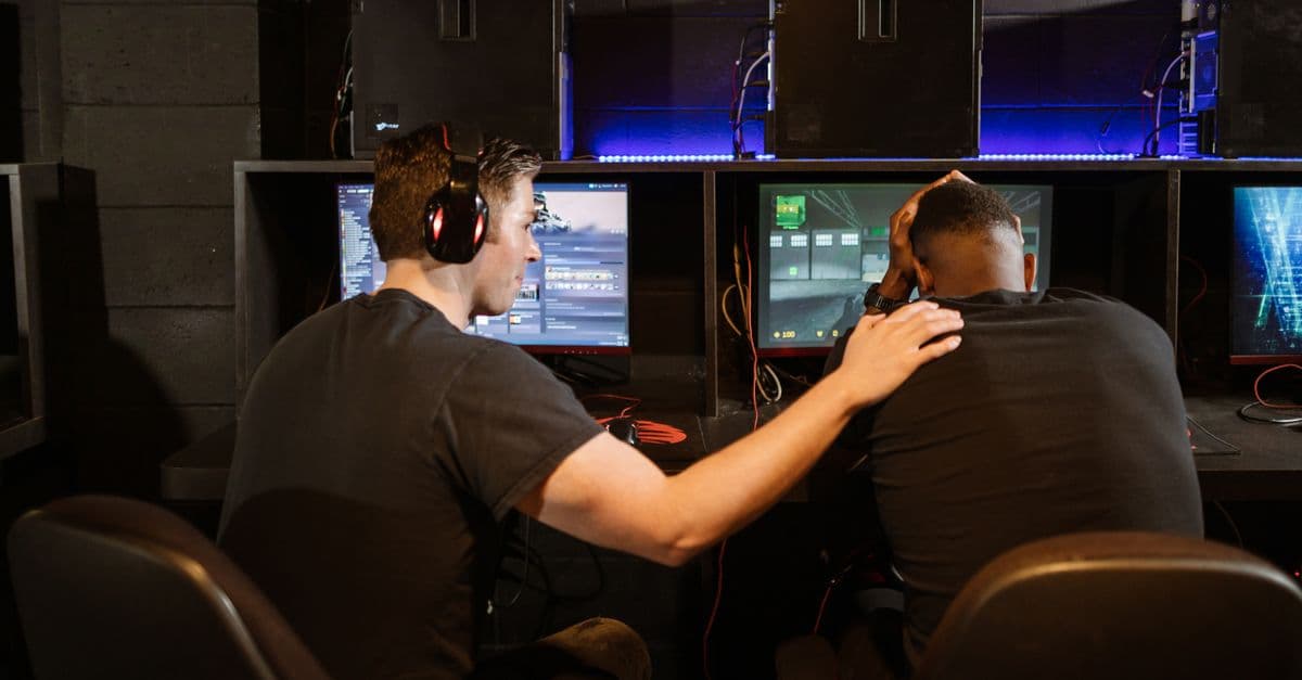 Two gamers support each other in a cyber cafe, navigating challenges together.