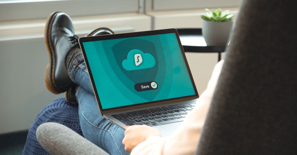A person wearing boots relaxes with a laptop displaying a VPN save screen indoors.