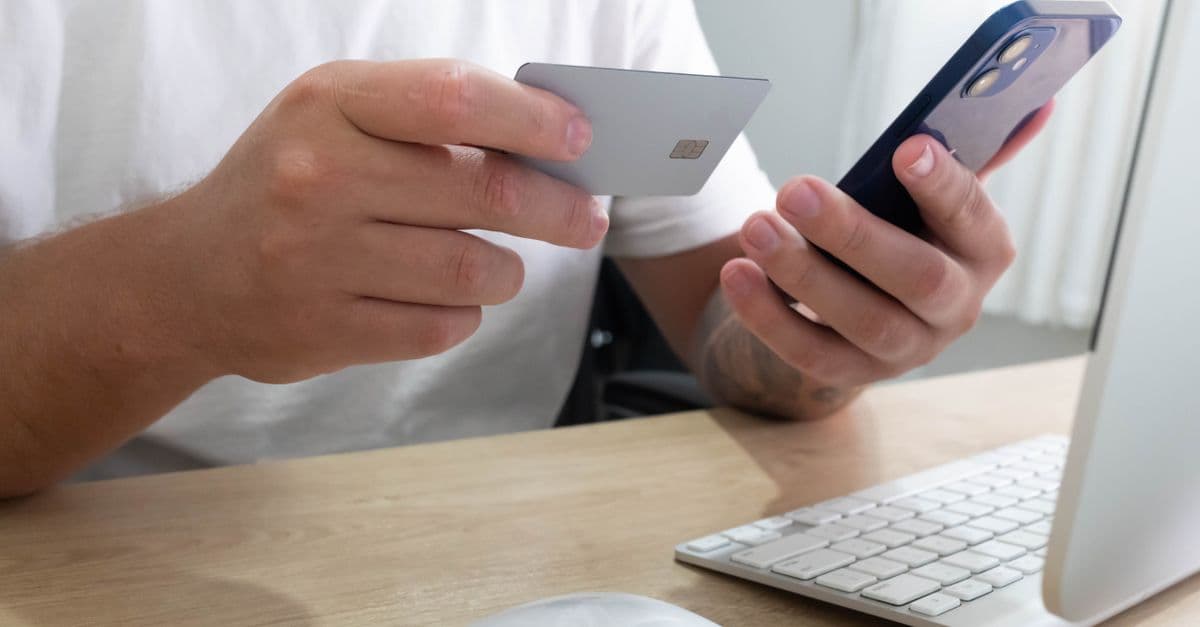 Person holding credit card and smartphone for an online transaction at a desk.