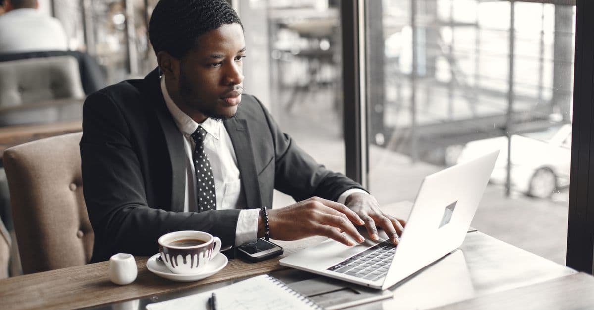 Adult man in a suit using a laptop at a café table with coffee.