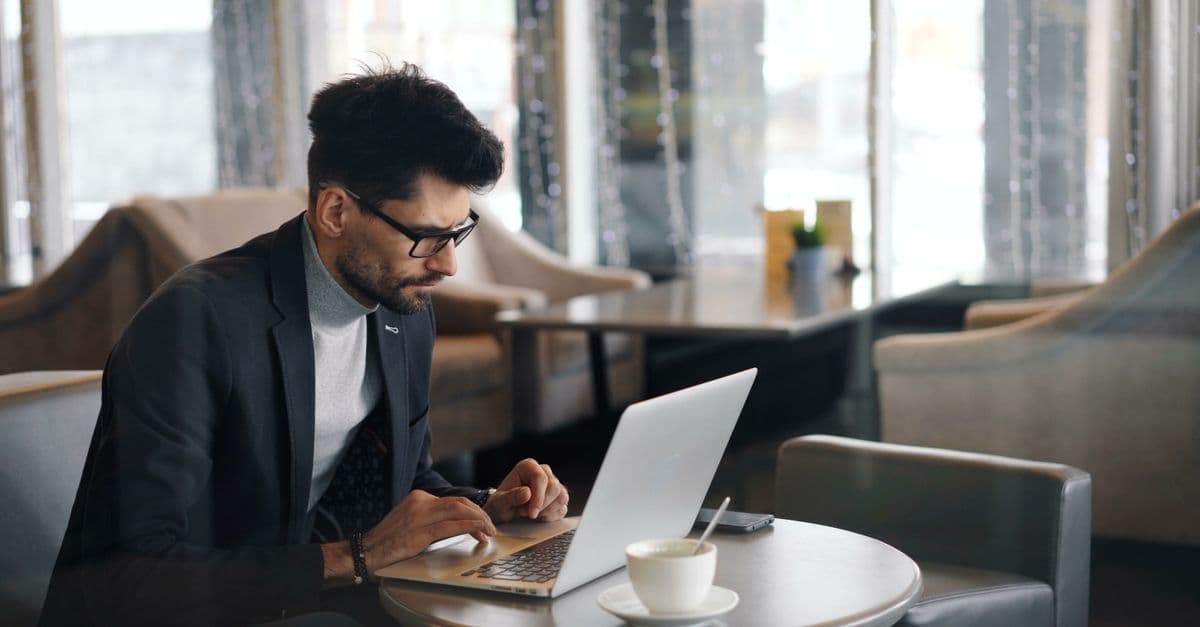 A stylish man in a cafe working on a laptop with coffee and modern decor.