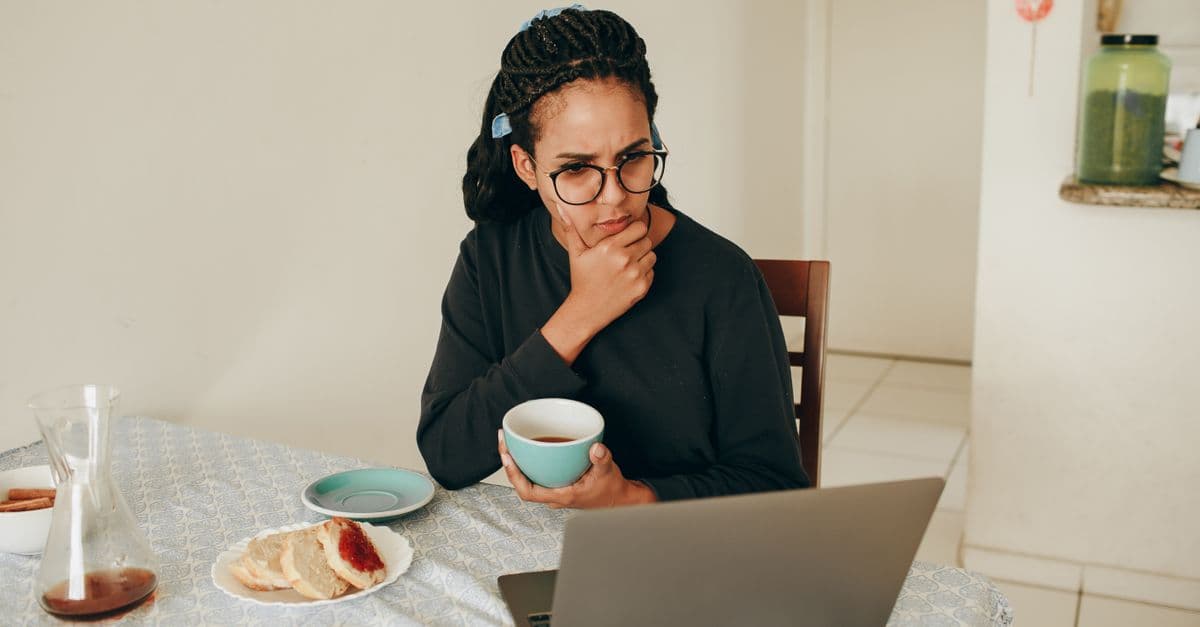 A woman sips coffee while intently focused on her laptop, indoors.