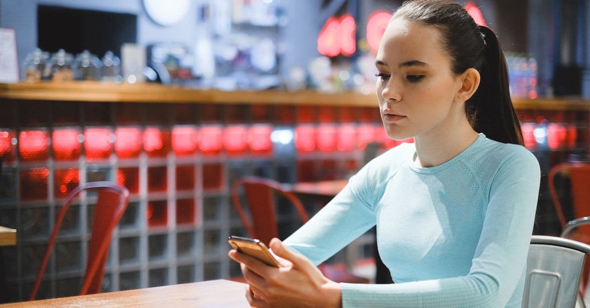 A young woman in a casual setting using a smartphone inside a trendy cafe.