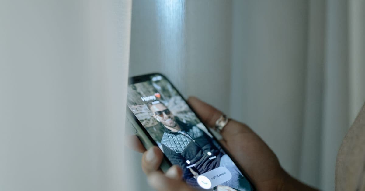 A hand holding a smartphone showing an incoming call notification with a photo of a man on the screen.