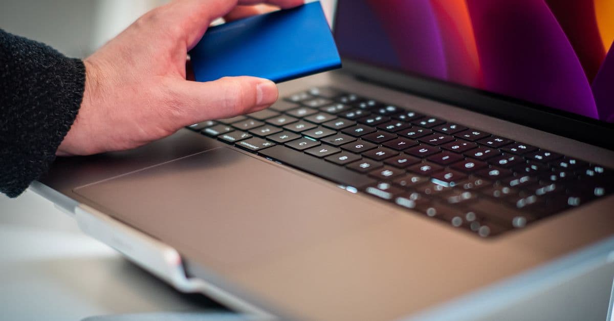 Close-up of a hand holding an external hard drive over a laptop keyboard.