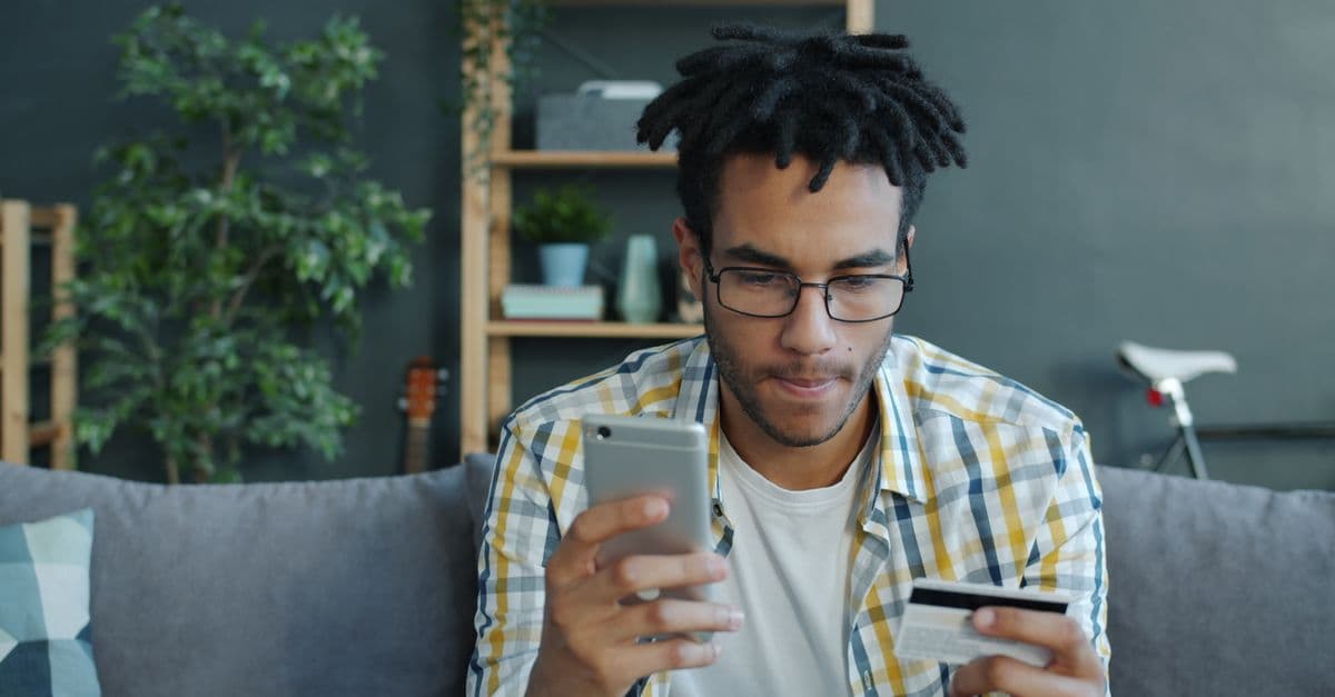 Young man using smartphone and credit card for secure online shopping at home.