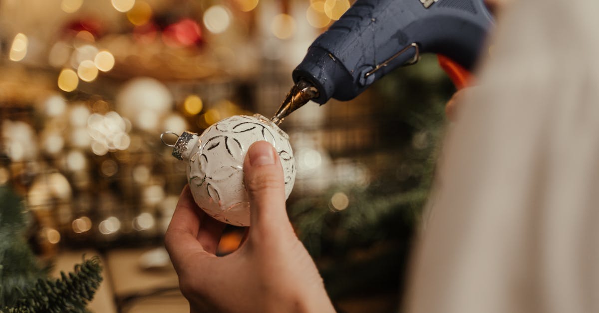 Close-up of hands using a glue gun to decorate a Christmas ornament. DIY holiday craft.