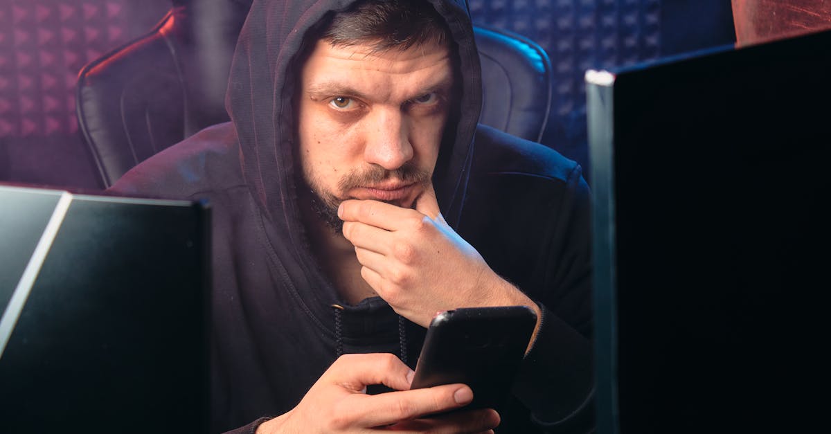 A man in a black hoodie contemplating while using a smartphone, surrounded by digital screens.