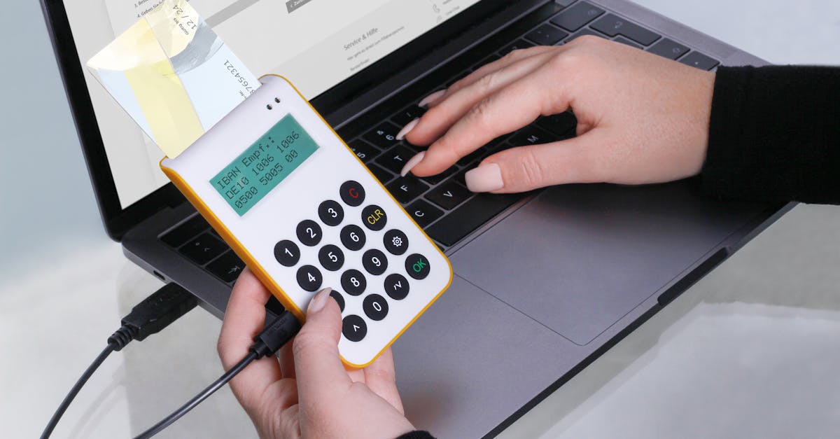 Close-up of hands using a card reader for online transactions via laptop, showcasing cashless payment technology.