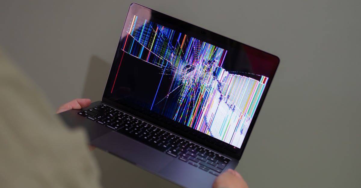 A broken laptop screen displayed with colorful glitch being held by a person.