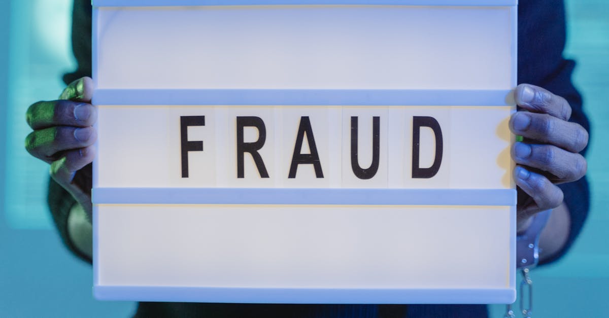 Close-up of hands holding a sign with 'fraud', illuminated in blue light.
