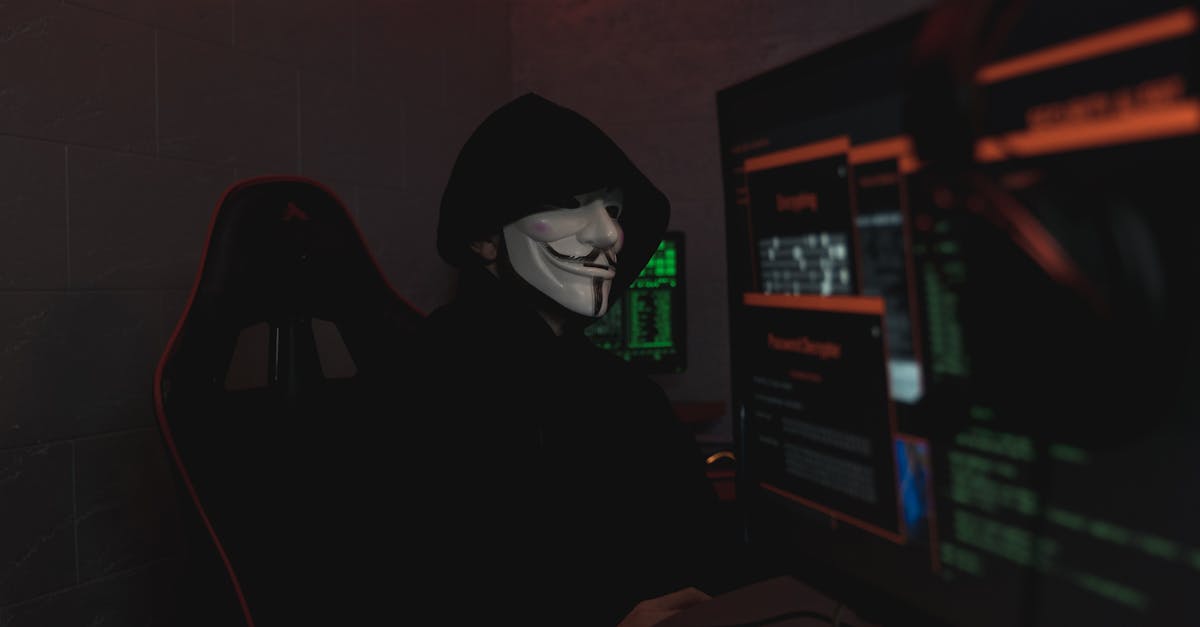 An anonymous hacker wearing a mask working on a computer in a dark room.