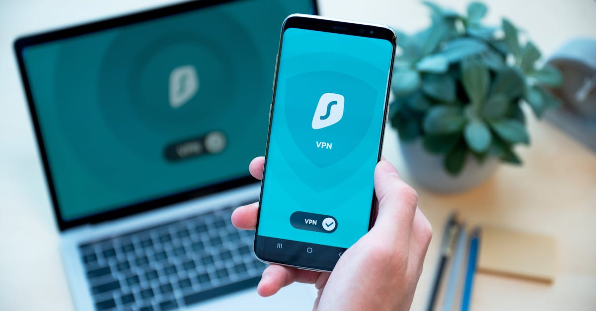 Close-up of a hand holding a smartphone with VPN app, laptop in the background, showcasing digital security.